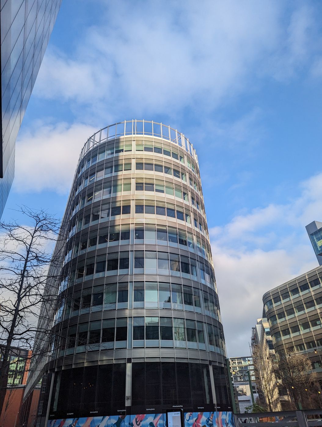 A curved, silver-louvred office tower in Spinningfields under scattered cloud