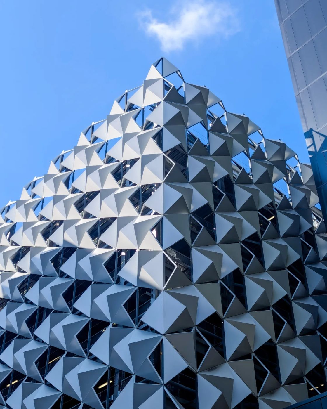 A folded, faceted silver metal facade rising into a blue sky
