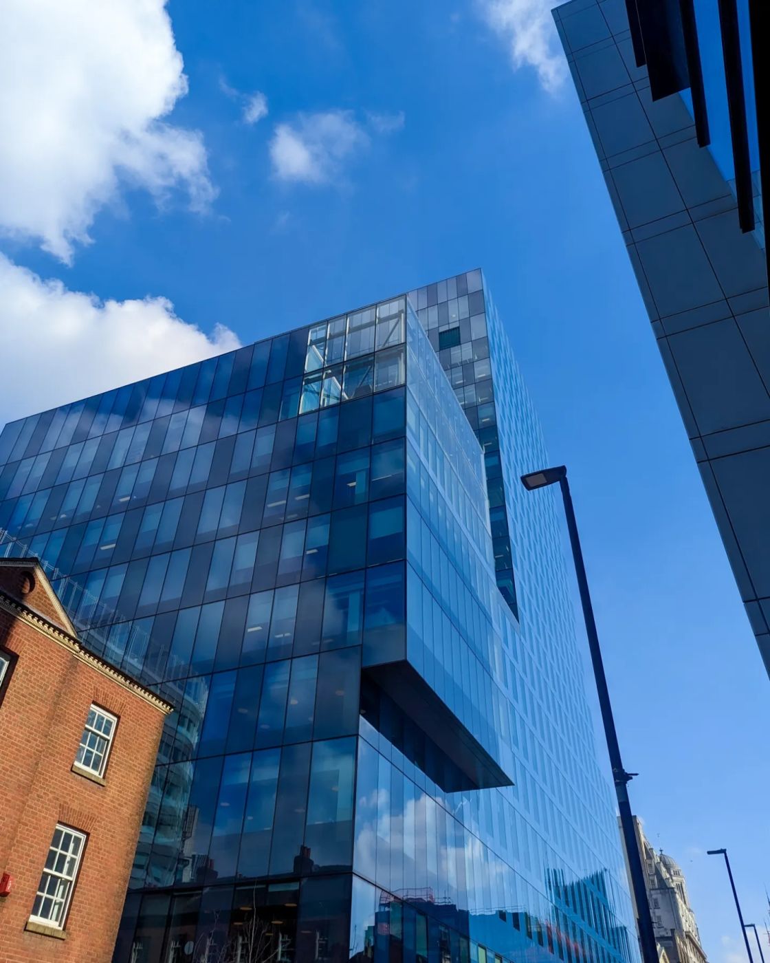 A glass tower with a cantilevered upper section beside an older brick building