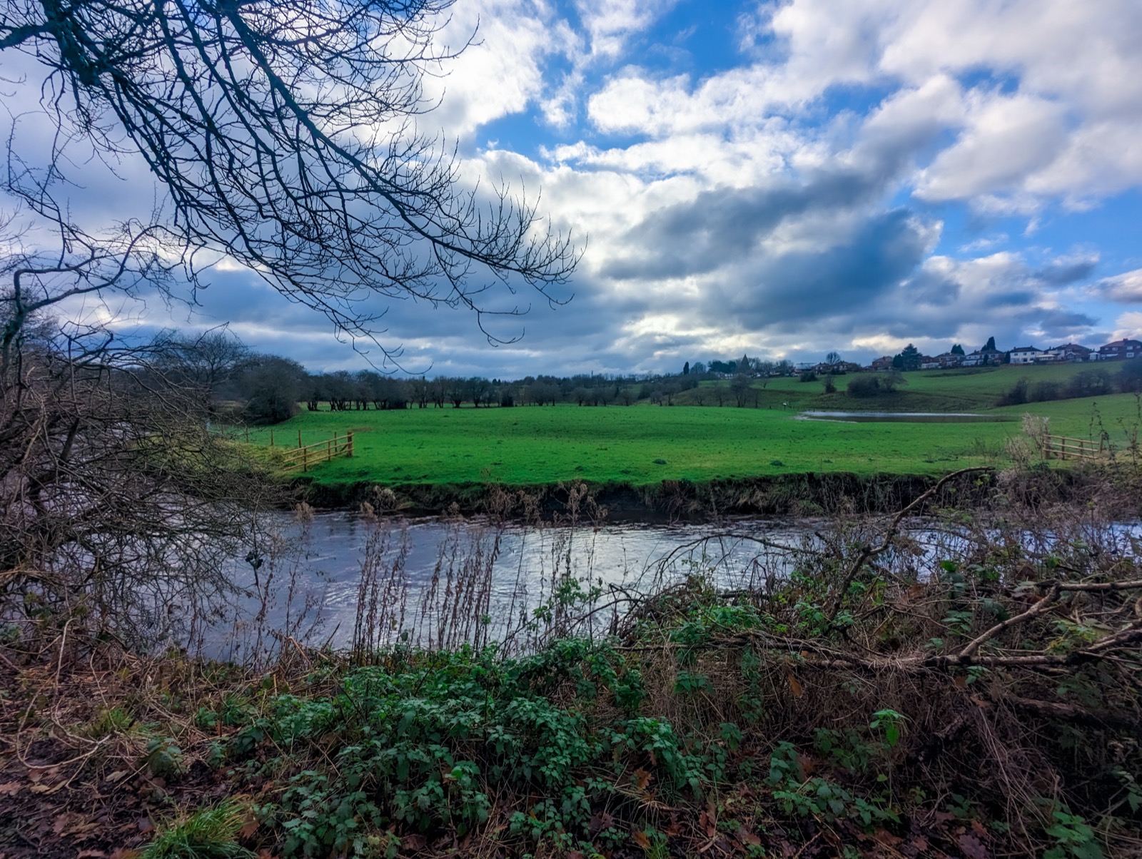 A river bending through open green fields under a big cloudy winter sky