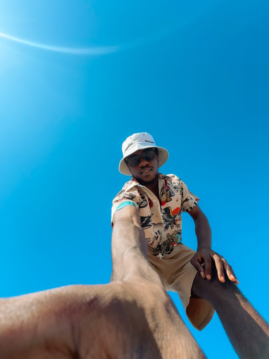 Me outdoors on a bright day in a bucket hat and sunglasses, shot from below against a deep blue sky