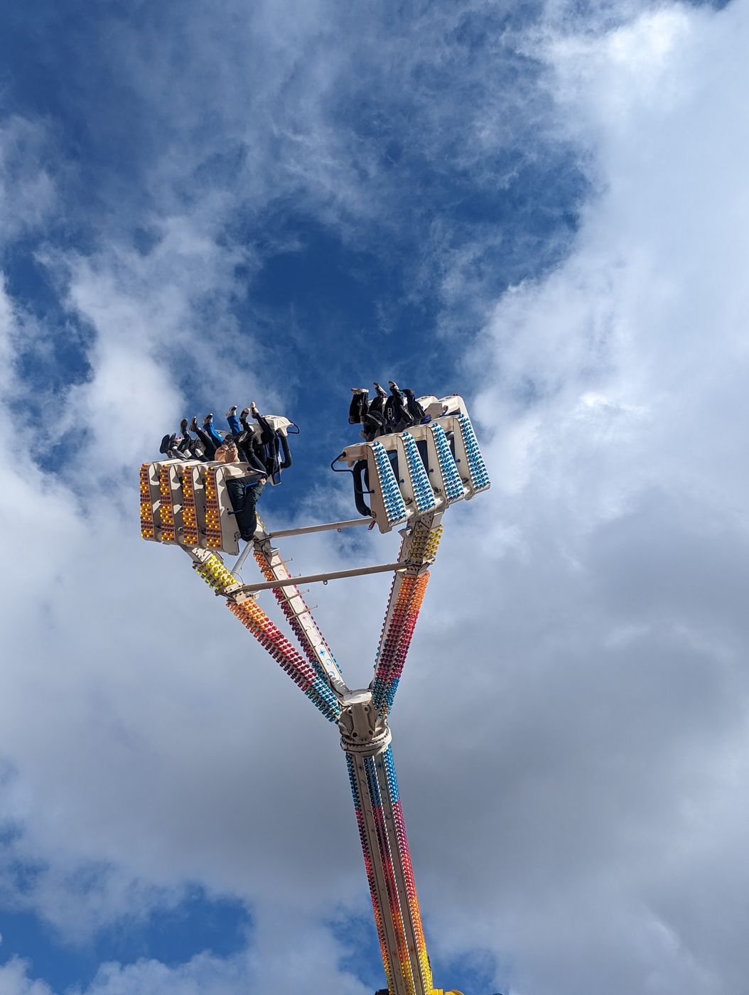 Looking up at a spinning fairground ride mid-swing against a blue, cloudy sky